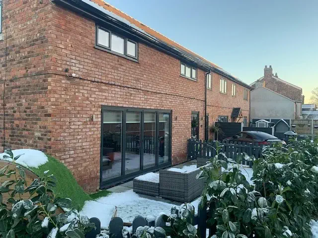 a wall-bricked house with a bi-fold black doors on a snowy day