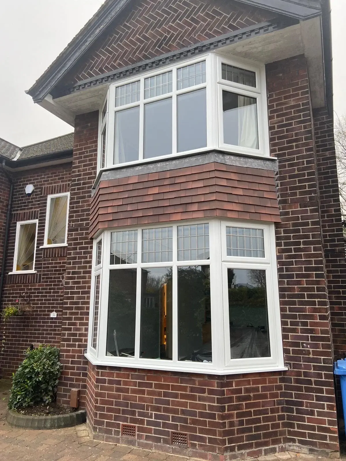 A two-story house with brown brick and white-framed UPVC windows, including a bay window on the ground floor, is shown.