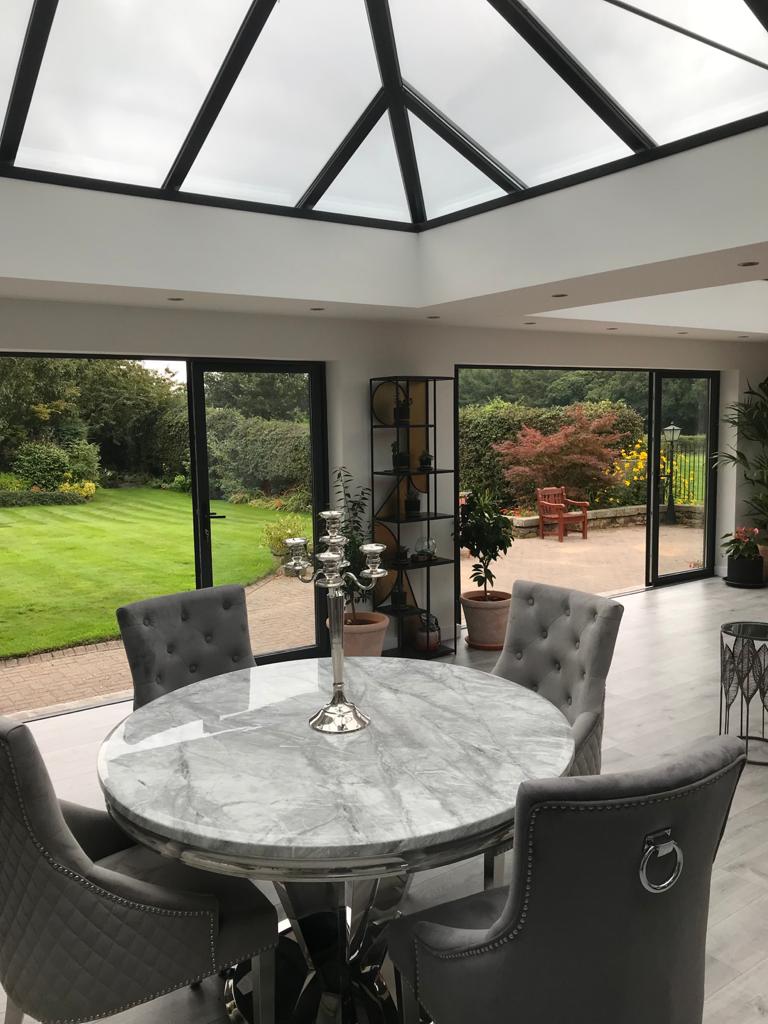 A dining room featuring a glass roof, elegantly furnished with a table and chairs, inviting natural light indoors.