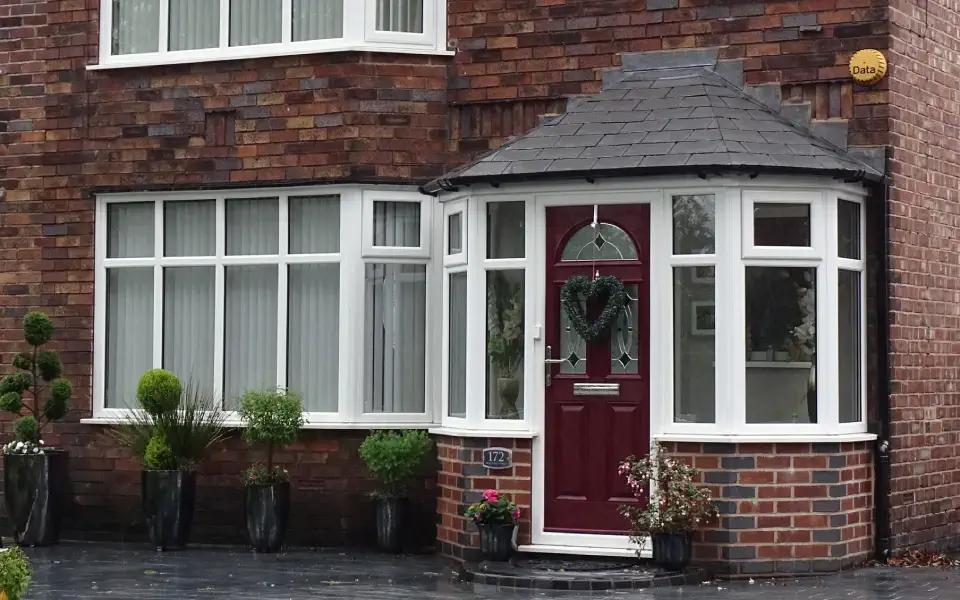 a wall-bricked house with a red front door and white-framed window glass